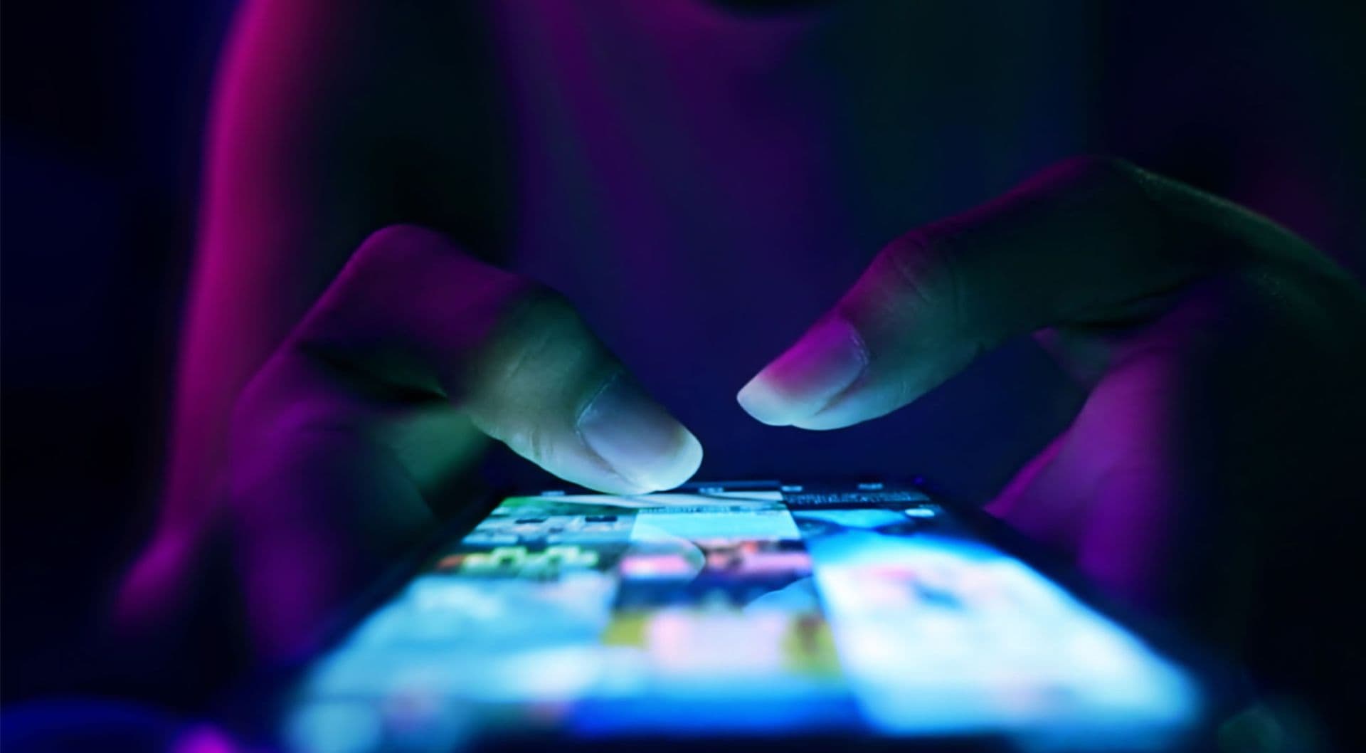 Close-up of hands using a smartphone screen under vibrant neon purple and blue lighting.
